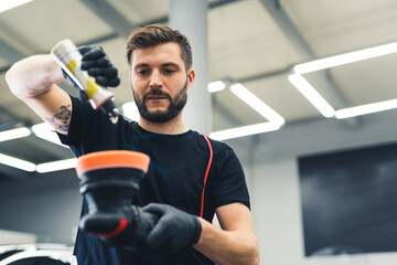 Caucasian man wearing black gloves preparing his professional buffer tool to polish fresh car...