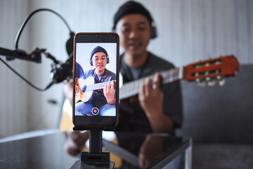 Asian influencer playing guitar during podcast or live video broadcast for the audience, recorded...