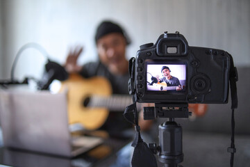Asian influencer playing guitar during podcast or live video broadcast for the audience, recorded from digital camera at home