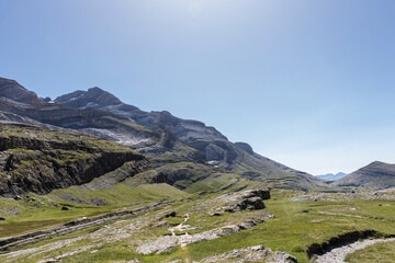 Fototapeta premium Green landscape in the pyrenees with layered mountains, green meadow and flowers, blue sky with clouds and path