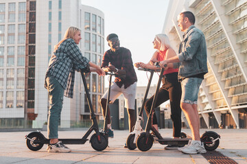 interracial group of young friends stand with electric scooters in the city and communicate, multiracial youth use electric transport