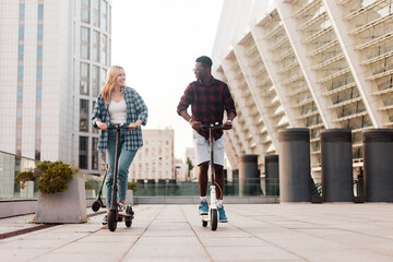 multiracial couple riding electric scooters in the city and smiling, afro american guy talking to european girl © Богдан Маліцький