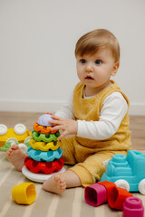Fototapeta na wymiar A cute child is playing with a colorful rainbow toy pyramid. Toys for small children.
