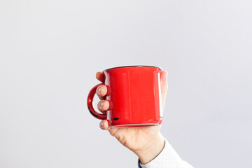 Close up of a person's hand holding a red coffee cup on a white background.