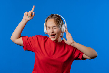 Happy teenager listening music, enjoying dance with headphones on blue