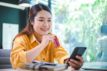 Young woman holding credit card and using laptop computer. Businesswoman working at cafe. Online shopping, e-commerce, internet banking, spending money