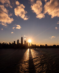 Naklejka na ściany i meble Beautiful downtown Chicago skyline aerial drone photograph above Lake Michigan during the autumn equinox sunset as the sun casts a glistening yellow glow and long building shadows over the water.