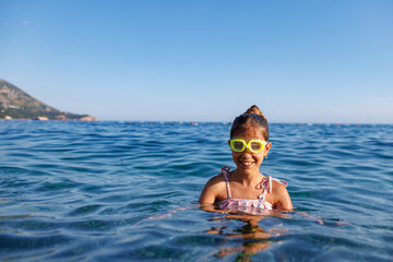Portrait of a girl in a bright swimsuit with children's goggles for swimming in the sea