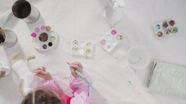 Flat lay. Little girl painting paper mache figurine at homeschooling art class.
