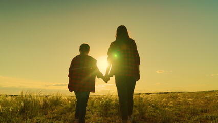 Happy family, mom, daughter hold hands walk together in acre in autumn. Active lifestyle. Mother, daughter, child go hand in hand at sunset in field. Parent, girl, child, happy childhood, Motherhood.