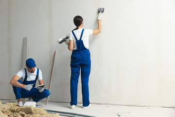 Professional workers plastering wall with putty knives indoors