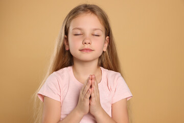 Girl with clasped hands praying on beige background