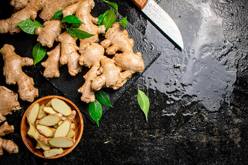 Pieces and whole ginger on a stone board with foliage. 
