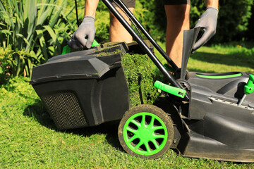 Man removing grass out of lawn mower box in garden, closeup