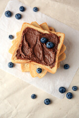 Tasty toast with chocolate paste and blueberries on parchment paper, flat lay