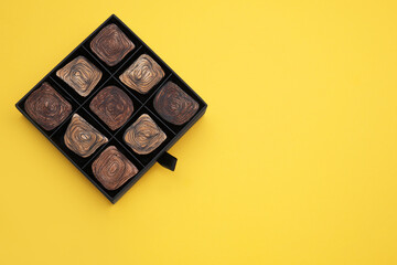 Box of tasty chocolate candies on yellow background, top view. Space for text