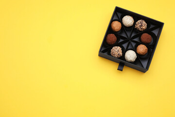 Box of tasty chocolate candies on yellow background, top view. Space for text