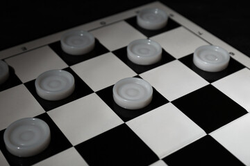 Checkerboard with game pieces on dark background, closeup