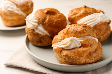 Delicious profiteroles with cream filling on table, closeup