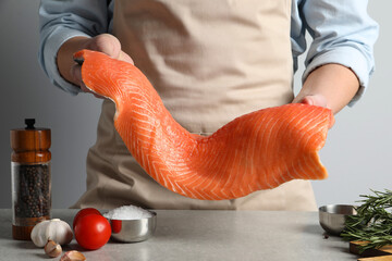 Man with raw salmon fillet at grey table, closeup