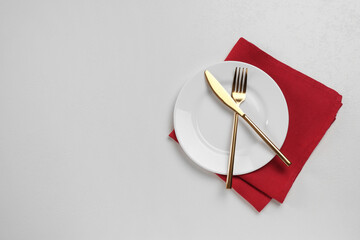 Clean plate and golden cutlery on white table, flat lay. Space for text