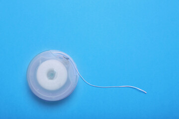 Container with dental floss on light blue background, top view. Space for text