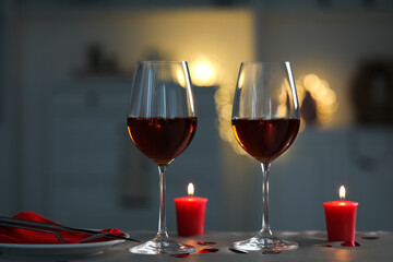 Romantic table setting with glasses of red wine and burning candles against blurred lights