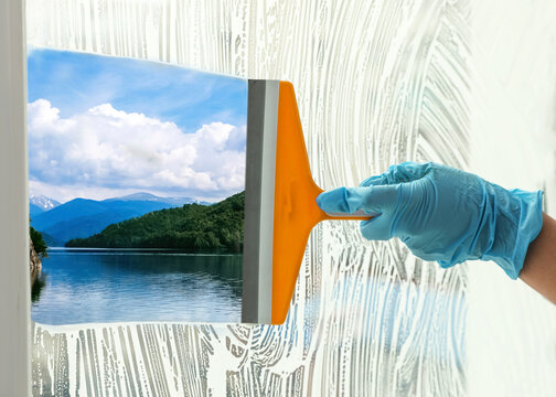 Worker cleaning window with squeegee, closeup. Picturesque river and mountains on sunny day, view through clear glass