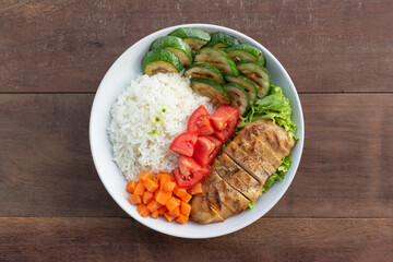 Healthy food grilled chicken has rice zucchini carrot tomato in plate on wood table.