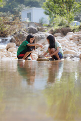 Two asian siblings playing sand nearing the river together with fun. Outdoor activity for children on vacation.