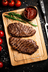 Grilled steak on a cutting board with rosemary and tomatoes. 
