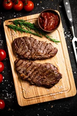 Poster Grilled steak on a cutting board with rosemary and tomatoes.  © Artem Shadrin