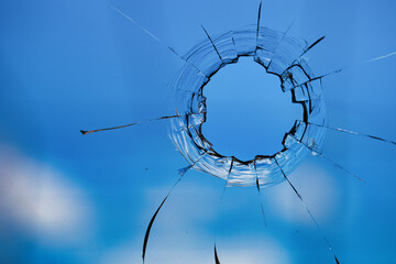 Bullet holes in the glass on the background of the blue sky.
