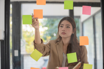 Asian businesswomen use post-it notes on glass walls to write strategy business plans to development grow to success