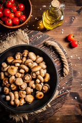 Frying pan with fried mushrooms on a wooden tray. 