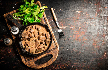 Liver in a frying pan on a cutting board with parsley and spices. 