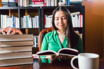 Young woman reading books indoor in her personal library, with a coffee mug. World book day