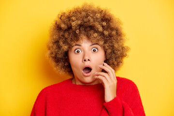 Worried woman looks nervously starring with scare look, has curly hair, anticipates what end will...
