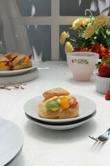 serving of eclairs with cream and pieces of fruit on a white plate with a cup of tea