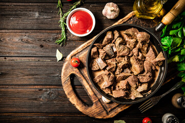 Fried liver in a frying pan on a cutting board with tomato sauce.