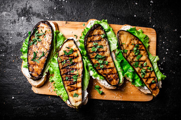 Sandwich with grilled eggplant and lettuce on a wooden cutting board. 