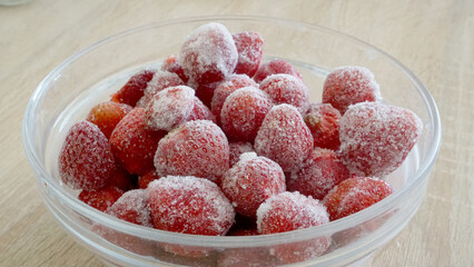 Glass bowl of frozen ripe red strawberries placed on light wooden table    