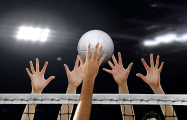 Close up of Volleyball player spiking and hand blocking over the net under bright spotlights