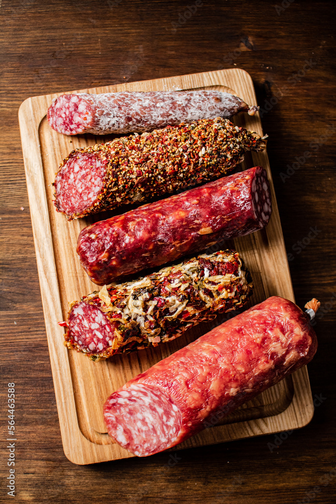 Poster different types of salami sausage on a wooden cutting board.