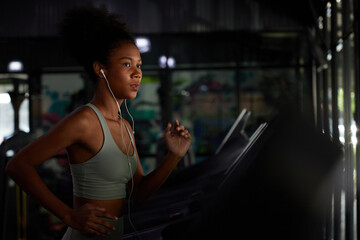 young sports woman working out with wired earbuds and running on treadmill in gym