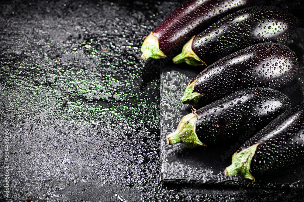 Wall mural Fresh ripe eggplant with droplets of water on a stone board. 