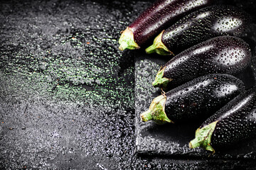 Fresh ripe eggplant with droplets of water on a stone board. 