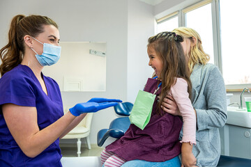 dentist woman in medical clothes checks teeth of baby girl to avoid caries.