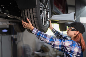 Female mechanic adjusting the tire of the car that is on the lift. A girl at a man's work.