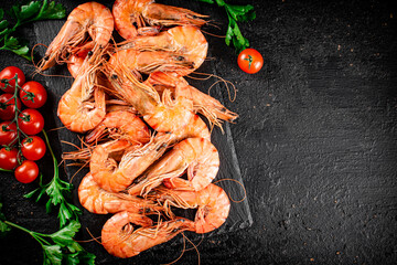 Boiled shrimp on a stone board with tomatoes and parsley.